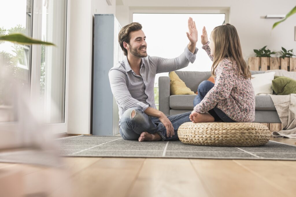 Young man and little girl sitting at home, giving high five